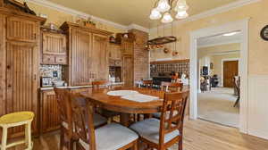 Dining area featuring light wood-type flooring, ornamental molding, a notable chandelier, and a wainscoted wall