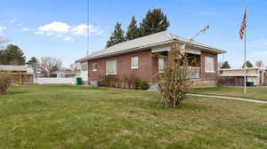 View of side of home with fence, a lawn, brick, and metal roof