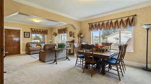 Carpeted dining room with arched walkways, baseboards, a textured ceiling, and ornamental molding