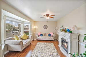 Living area with wood finished floors, ceiling fan, a glass covered fireplace, and a textured ceiling