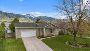 Ranch-style home featuring concrete driveway, a front yard, a mountain view, fence, and a garage