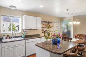 Kitchen featuring dark countertops, a kitchen bar, white dishwasher, and a sink
