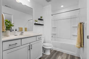 Bathroom with visible vents, shower / bath combo with shower curtain, toilet, wood finished floors, and vanity