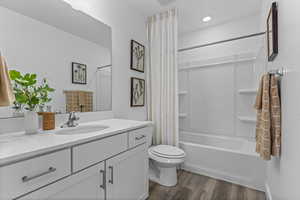 Bathroom with wood finished floors, toilet, shower / bath combination with curtain, and vanity