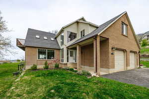 Traditional home featuring brick siding, aphalt driveway, a garage, roof with shingles, and a front lawn