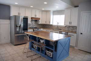 Kitchen with a sink, stainless steel appliances, open shelves, tasteful backsplash, and wooden counters