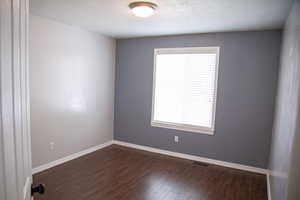 Spare room featuring dark wood-type flooring, visible vents, baseboards, and a healthy amount of sunlight