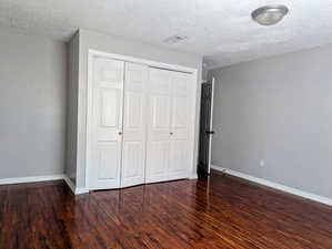 Unfurnished bedroom featuring a closet, wood finished floors, baseboards, and a textured ceiling