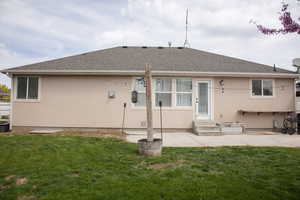 Rear view of house with stucco siding, a yard, entry steps, roof with shingles, and a patio area