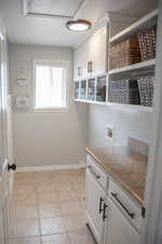 Laundry room featuring washer hookup, light tile patterned floors, cabinet space, and baseboards