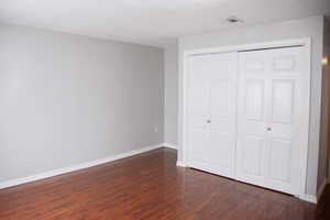 Unfurnished bedroom featuring dark wood-style floors, a closet, visible vents, baseboards, and a textured ceiling