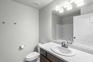 Bathroom with toilet, vanity, baseboards, visible vents, and a shower