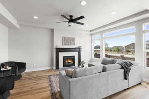 Living room with light wood-type flooring, a wealth of natural light, ceiling fan, and a glass covered fireplace