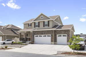 View of front of property featuring a garage, driveway, stone siding, roof with shingles, and stucco siding
