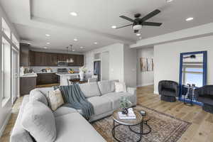 Living area featuring baseboards, light wood finished floors, recessed lighting, and ceiling fan with notable chandelier