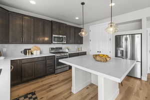Kitchen featuring light wood finished floors, dark brown cabinetry, stainless steel appliances, and tasteful backsplash