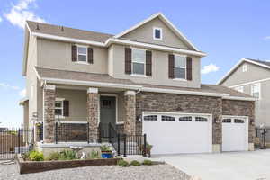 View of front of house featuring driveway, stone siding, stucco siding, and fence