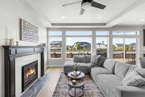 Living area with a fireplace, a tray ceiling, ceiling fan, and light wood-style floors