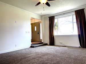 Spare room featuring carpet, crown molding, baseboards, and ceiling fan