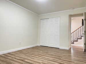 Unfurnished bedroom with baseboards, crown molding, light wood-style floors, and a closet