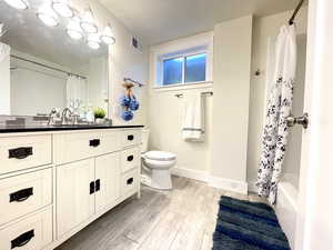 Full bathroom with toilet, baseboards, visible vents, wood finished floors, and vanity
