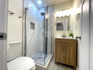 Full bath featuring wood finished floors, vanity, a shower stall, and toilet