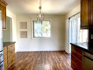 Unfurnished dining area featuring baseboards, an inviting chandelier, and dark wood-style flooring