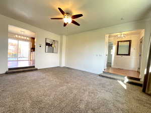 Carpeted spare room featuring ceiling fan with notable chandelier, baseboards, and ornamental molding