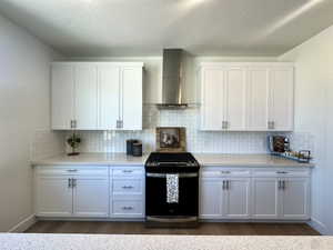 Kitchen featuring gas stove, wall chimney exhaust hood, dark wood-style floors, and light countertops