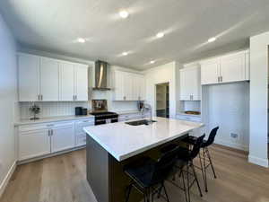 Kitchen with a sink, white cabinetry, baseboards, and wall chimney exhaust hood