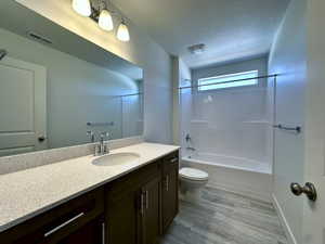 Full bath with wood finished floors, toilet, vanity, visible vents, and a textured ceiling