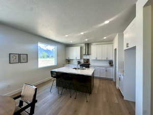 Kitchen featuring white cabinetry, a sink, light countertops, a kitchen bar, and wall chimney exhaust hood