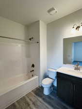 Bathroom with wood finished floors, bathtub / shower combination, toilet, vanity, and visible vents