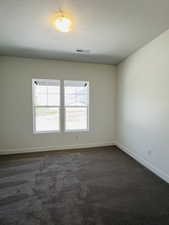 Empty room with a textured ceiling, visible vents, dark carpet, and baseboards