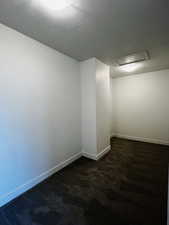 Unfurnished room featuring dark colored carpet and baseboards
