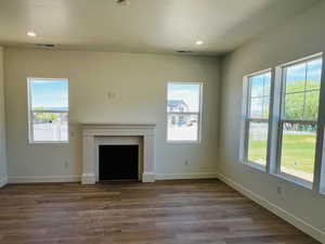 Unfurnished living room with baseboards, wood finished floors, a fireplace, and plenty of natural light