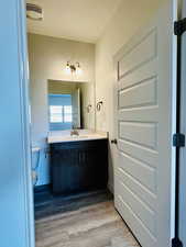 Bathroom featuring visible vents, wood finished floors, toilet, and vanity