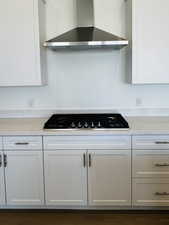 Kitchen with white cabinetry, light countertops, gas stovetop, and wall chimney exhaust hood