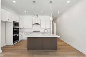 Kitchen with light wood-type flooring, white cabinetry, light countertops, recessed lighting, and a center island with sink