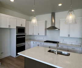 Kitchen featuring wood finished floors, white cabinets, black appliances, a sink, and wall chimney exhaust hood