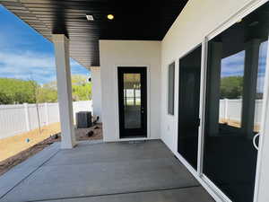 View of exterior entry with a patio, fence, stucco siding, and central air condition unit