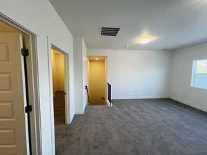 Unfurnished room featuring dark colored carpet, visible vents, and baseboards