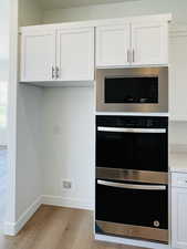 Kitchen featuring white cabinetry, built in microwave, dobule oven black, and light wood-type flooring