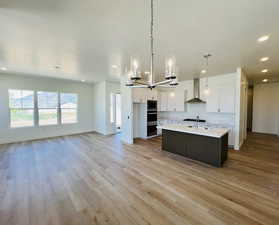 Kitchen featuring light countertops, white cabinets, baseboards, built in microwave, and wall chimney exhaust hood