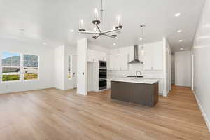Kitchen with light countertops, a chandelier, light wood-type flooring, white cabinets, and wall chimney range hood