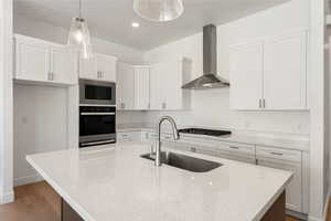 Kitchen featuring wall chimney range hood, stainless steel appliances, wood finished floors, white cabinetry, and light stone counters