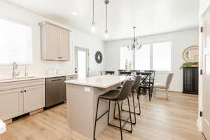 Kitchen with light wood finished floors, a sink, a breakfast bar, a kitchen island, and dishwasher