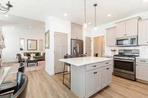 Kitchen with stainless steel appliances, light wood finished floors, a kitchen bar, and light countertops
