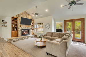 Living area with high vaulted ceiling, wood finished floors, a ceiling fan, a stone fireplace, and french doors
