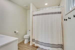 Full bath with wood finished floors, a shower with curtain, toilet, vanity, and visible vents